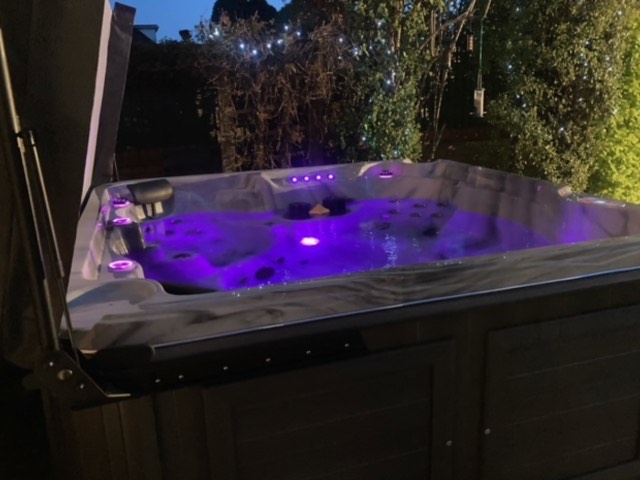 Hot tub fitted with colour-changing LED lighting in a garden at night