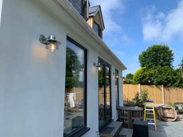 Exterior wall lights fitted along a rendered house with bifold doors